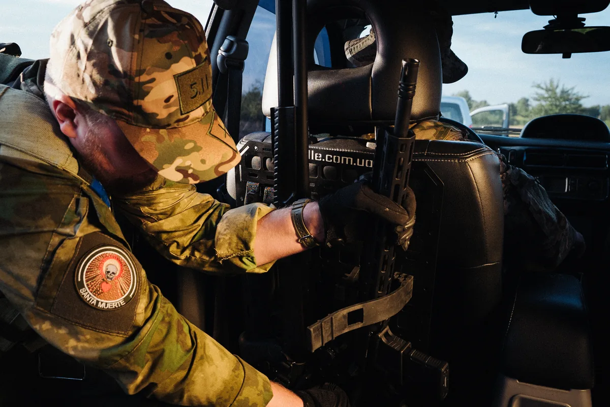 військовий виймає зброю з MOLLE панелі в авто