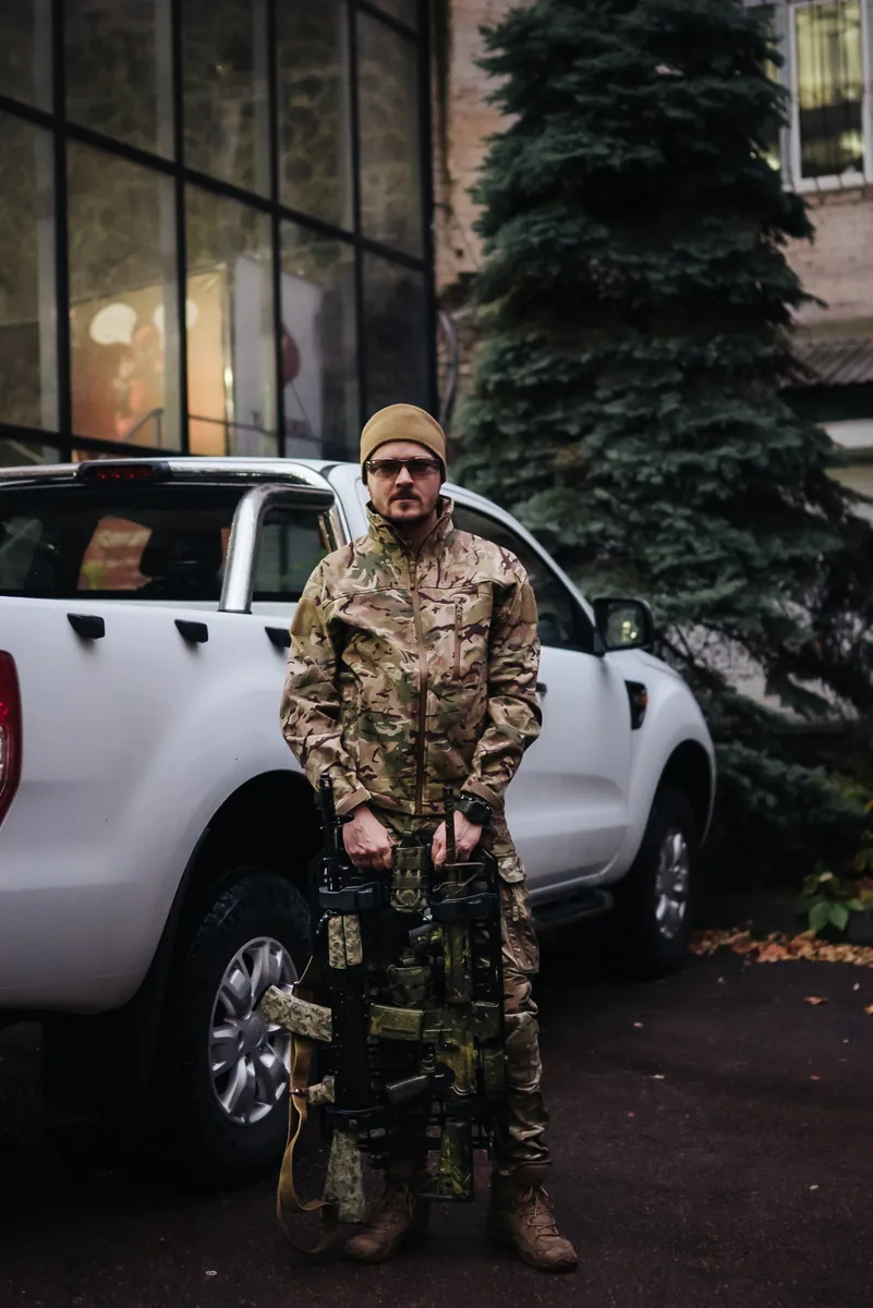 Військовий у мультикамі тримає MOLLE панель зі зброєю поруч із пікапом Ford Ranger